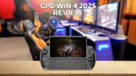 Μια εικόνα του μοντέλου GPD WIN 4 2025, που παρουσιάζει τη συμπαγή φορητή συσκευή παιχνιδιών με φυσικό πληκτρολόγιο και ενσωματωμένα χειριστήρια παιχνιδιών. Η συσκευή προβάλλεται σε μια ξύλινη επιφάνεια σε πρώτο πλάνο, ενώ στο βάθος εμφανίζεται μια θολή εγκατάσταση παιχνιδιού με πολλαπλές οθόνες και καρέκλες παιχνιδιού. Το κείμενο 'GPD WIN 4 2025 REVIEW' είναι εμφανώς τοποθετημένο στο πάνω μέρος της εικόνας.