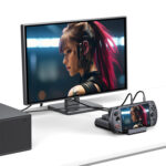 En skrivebordsopsætning, der viser GPD WIN 5 docket og tilsluttet en ekstern skærm via kabler. Det samme billede af en kvindelig figur med lyserødt hår vises på både den lille konsolskærm og den store eksterne skærm, hvilket demonstrerer dockens videoudgangskapacitet. 